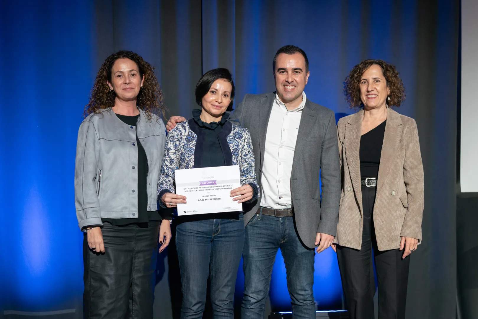 Els guanyadors posen amb el diploma del premi sobre l'escenari amb la presidenta del CETT, Maria Abellanet i la representant de la Diputació de Barcelona.